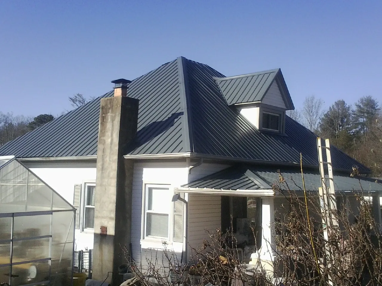 Dark blue standing seam metal roof on a white farmhouse with dormer — Slate & Tile Roof Repair by Roofing Brothers in Fleetville