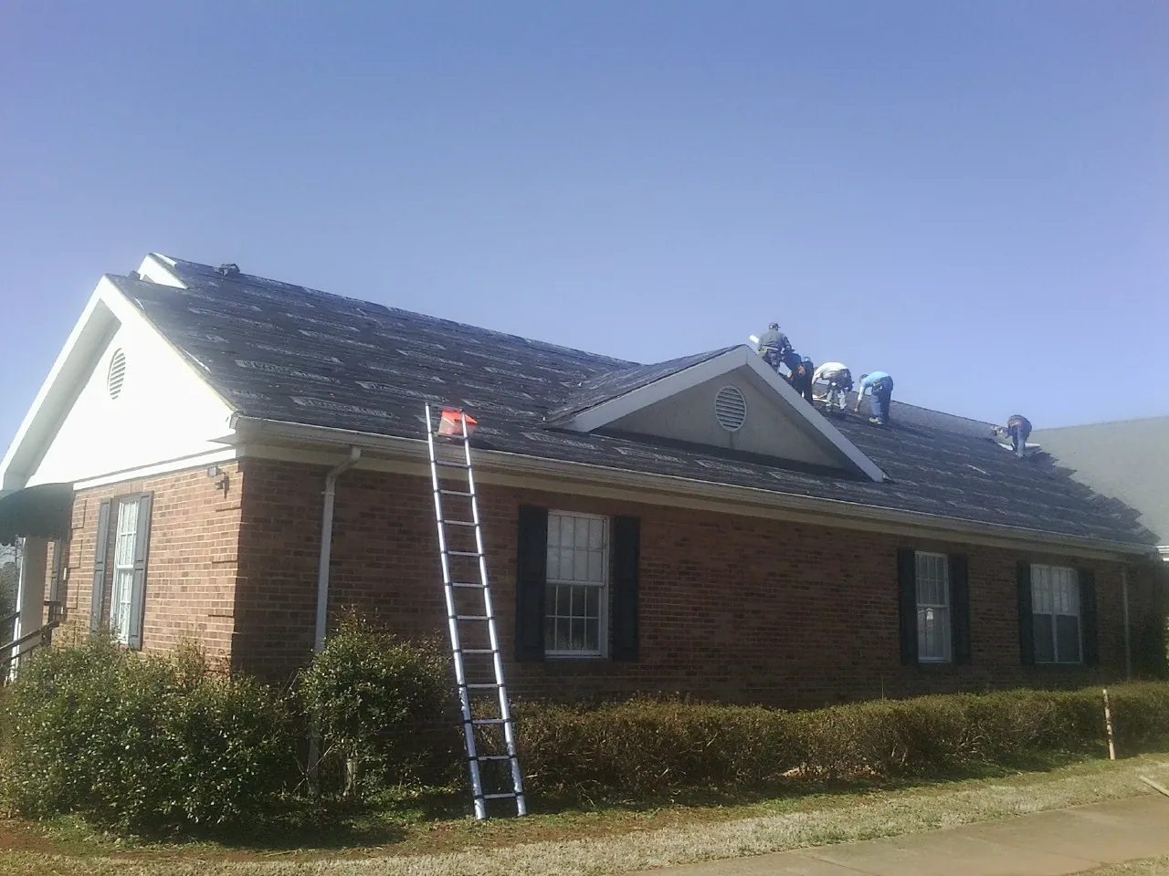 Crew tearing shingles off a brick ranch roof with a ladder set — Metal Roof Repair work by our crew in Fleetville