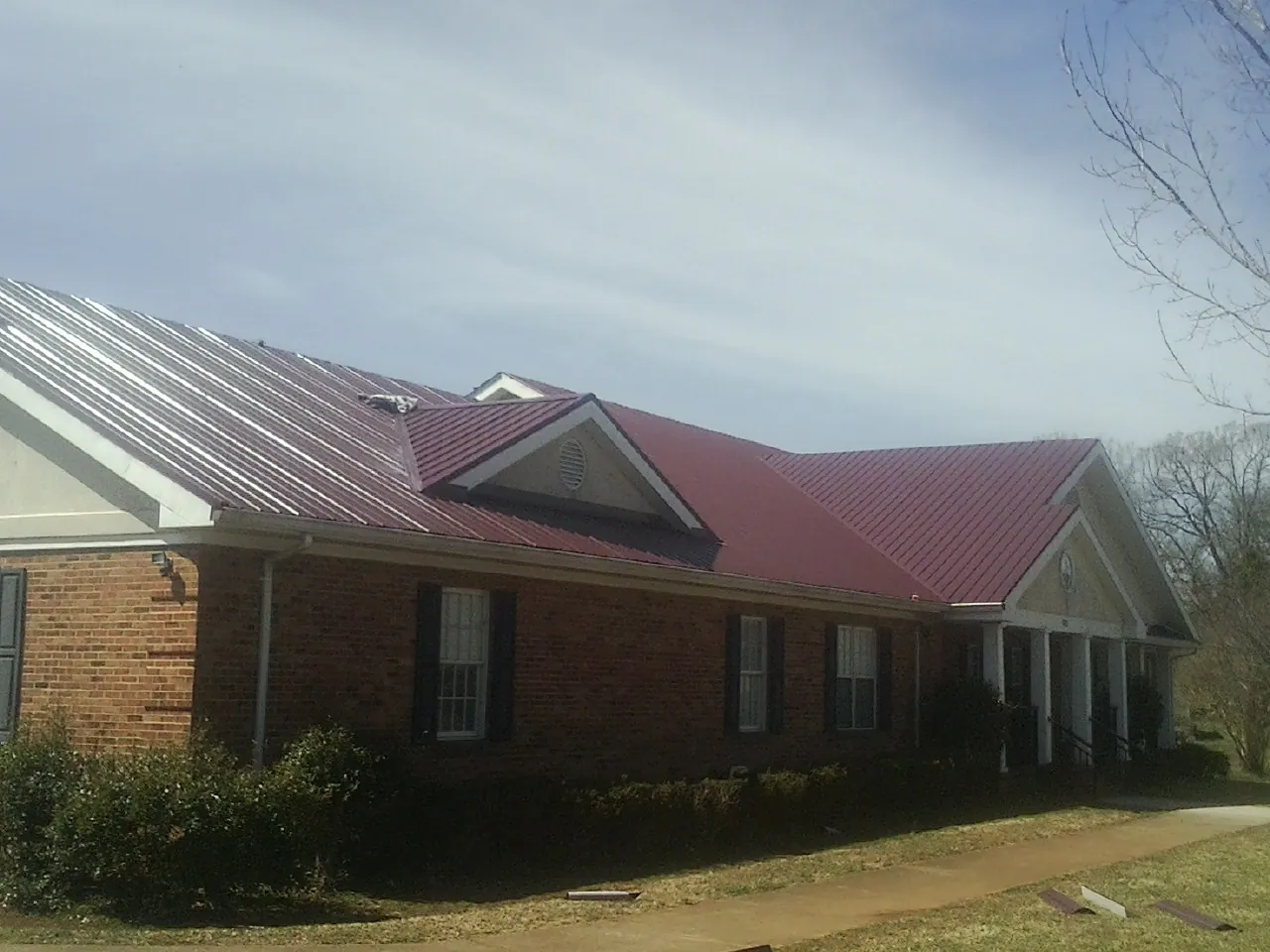 Red metal roof with gabled entries on a long brick building, from a Hail Damage Roof Repair job in Fleetville