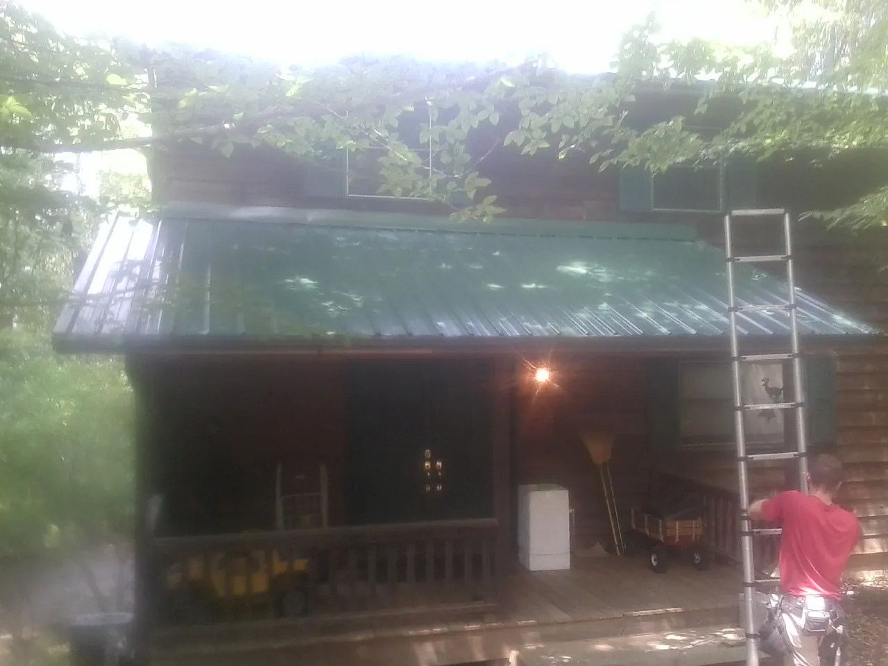 Worker on a ladder at the green porch roof of a wooded cabin in Fleetville