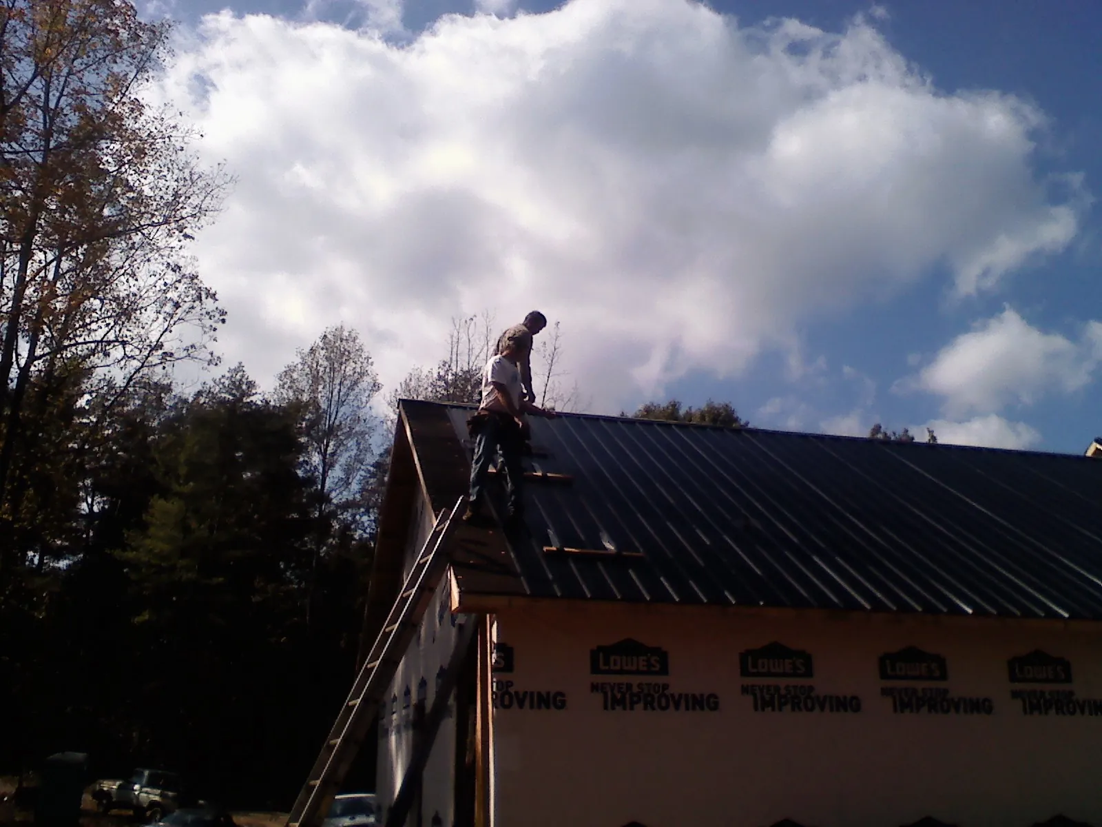 Roofer fastening dark metal panels high against a cloudy sky, from a Roof Inspection job in Fleetville