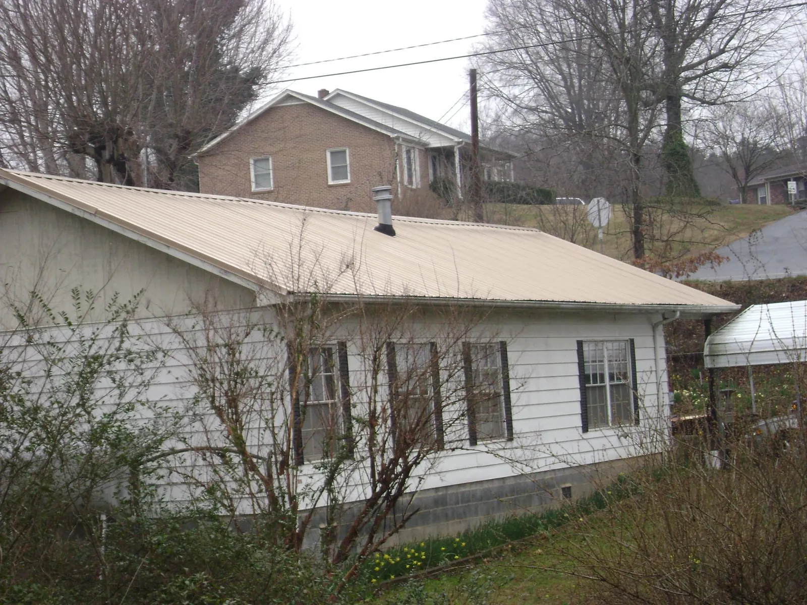 Tan metal roof on a white sided house set into a hillside — Commercial Roofing by Roofing Brothers in Fleetville